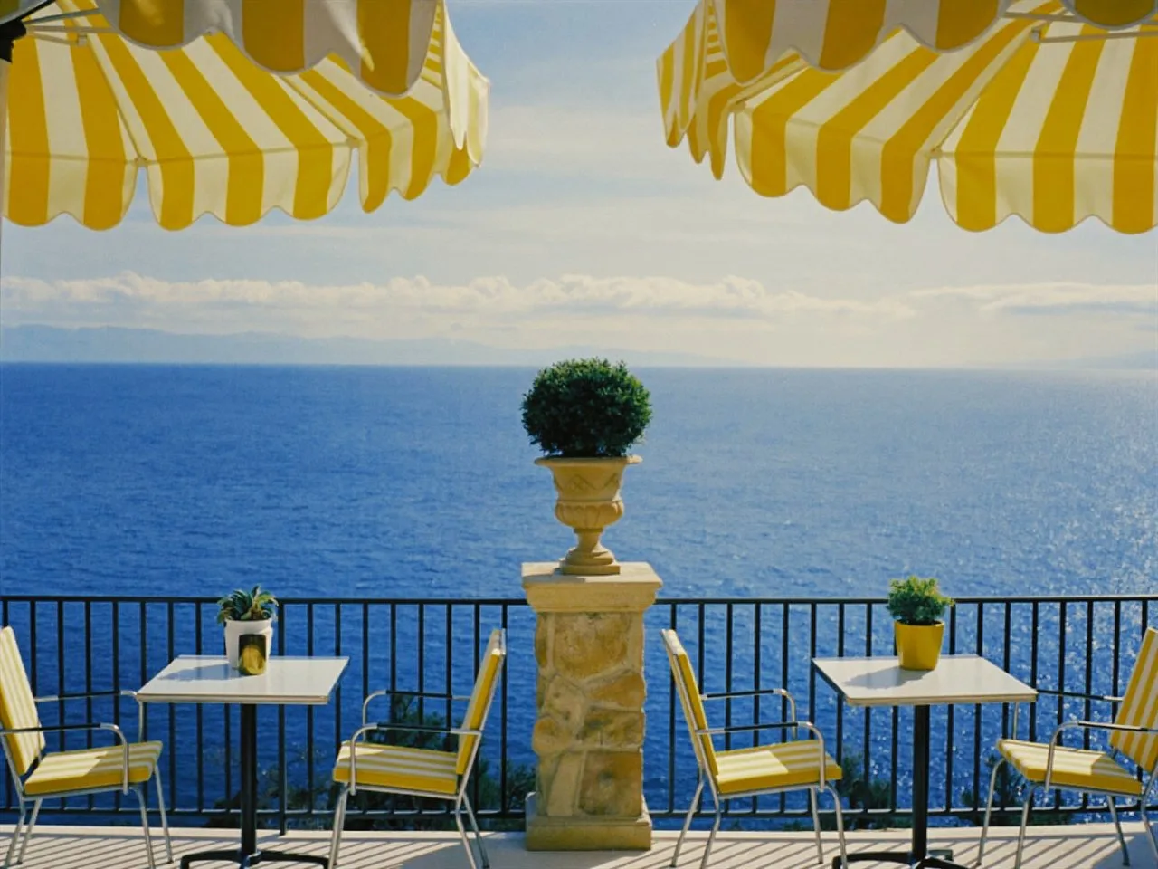Aureon 100 film stock in Chromogen, a vivid fine-grain negative: a seaside terrace under yellow striped umbrellas
