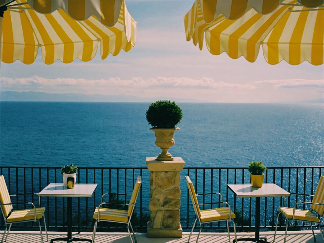 Solia 200 film stock in Chromogen, a golden warm lab scan: a seaside terrace under yellow striped umbrellas