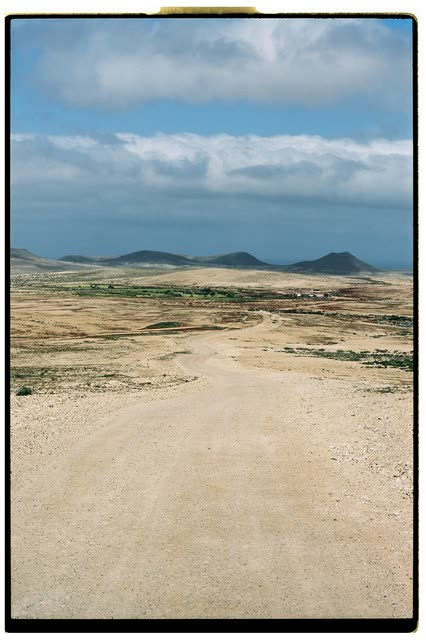 Location scout photo on a Chromogen moodboard: a dirt road through a volcanic desert