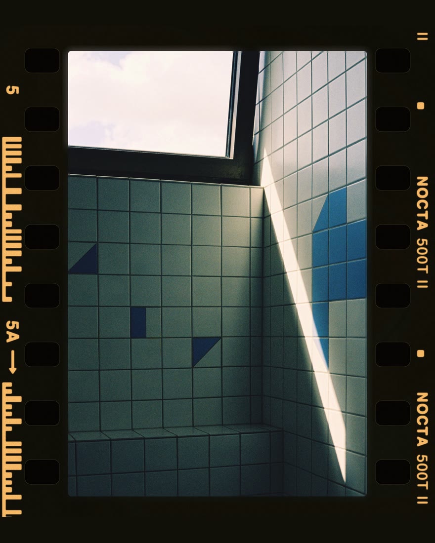 Chromogen Film border, 35mm strip: a tiled room with a shaft of sunlight on a strip of film with sprocket holes and edge printing