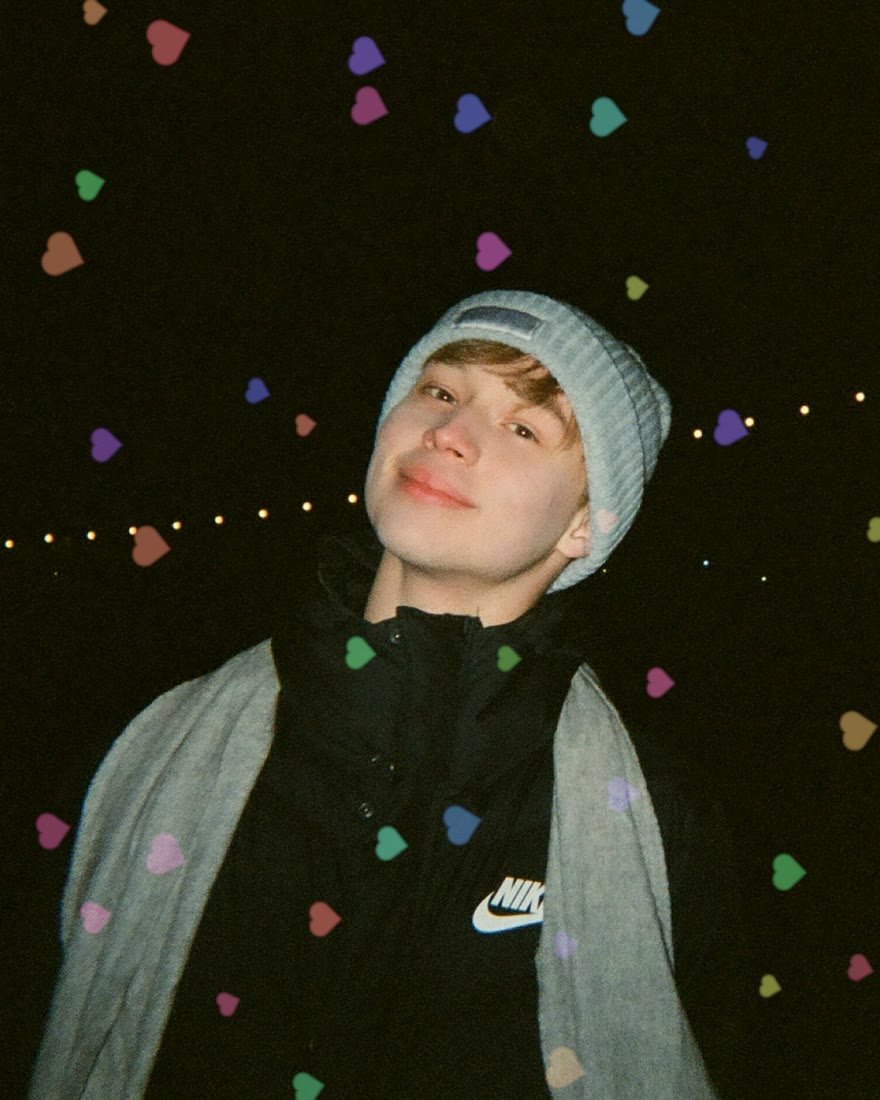 A smiling person in a grey beanie and scarf at night, with small coloured hearts pre-exposed across the dark